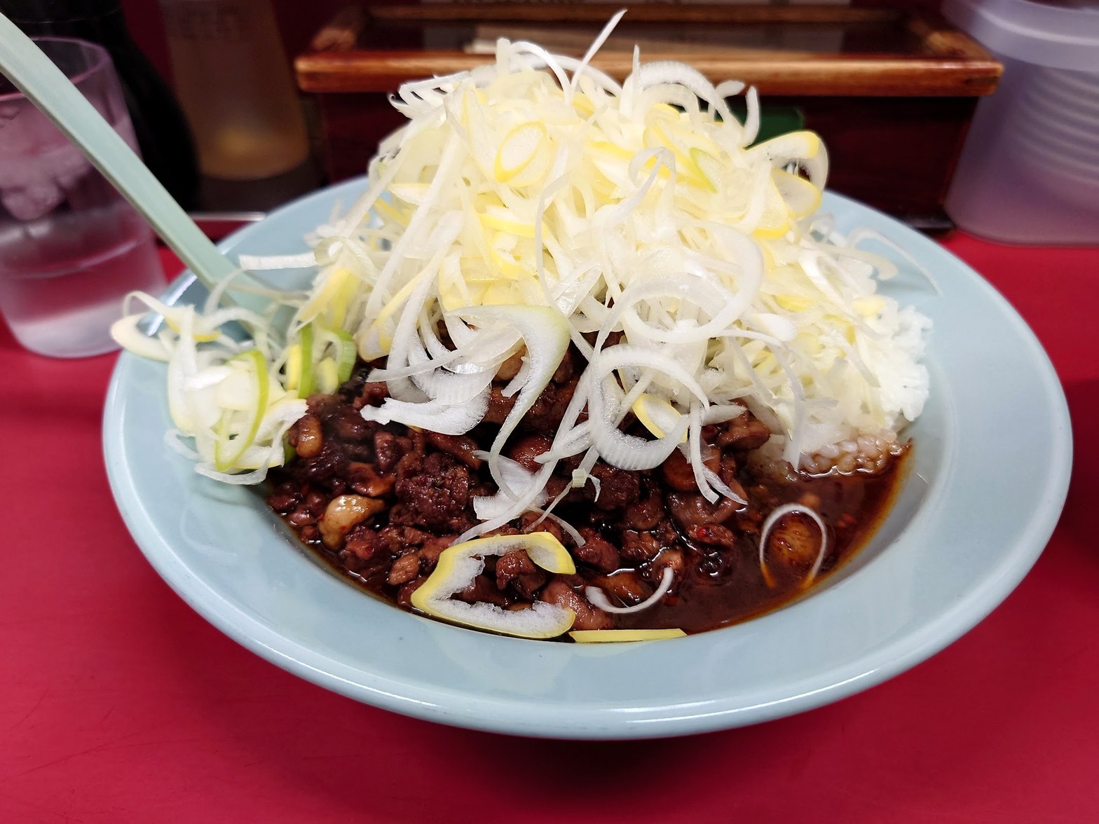 水色の丼に盛られた純レバ炒めと山盛りの白ネギ、赤いテーブルの上